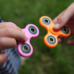 A closeup of two hands holding fidget spinners out toward each other