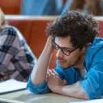 Bored Male Student Listens Lecture at the University. Tired, Exhausted and Overworked Young Male Holds His Head.