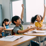 Several middle school students eagerly raise their hands to answer questions