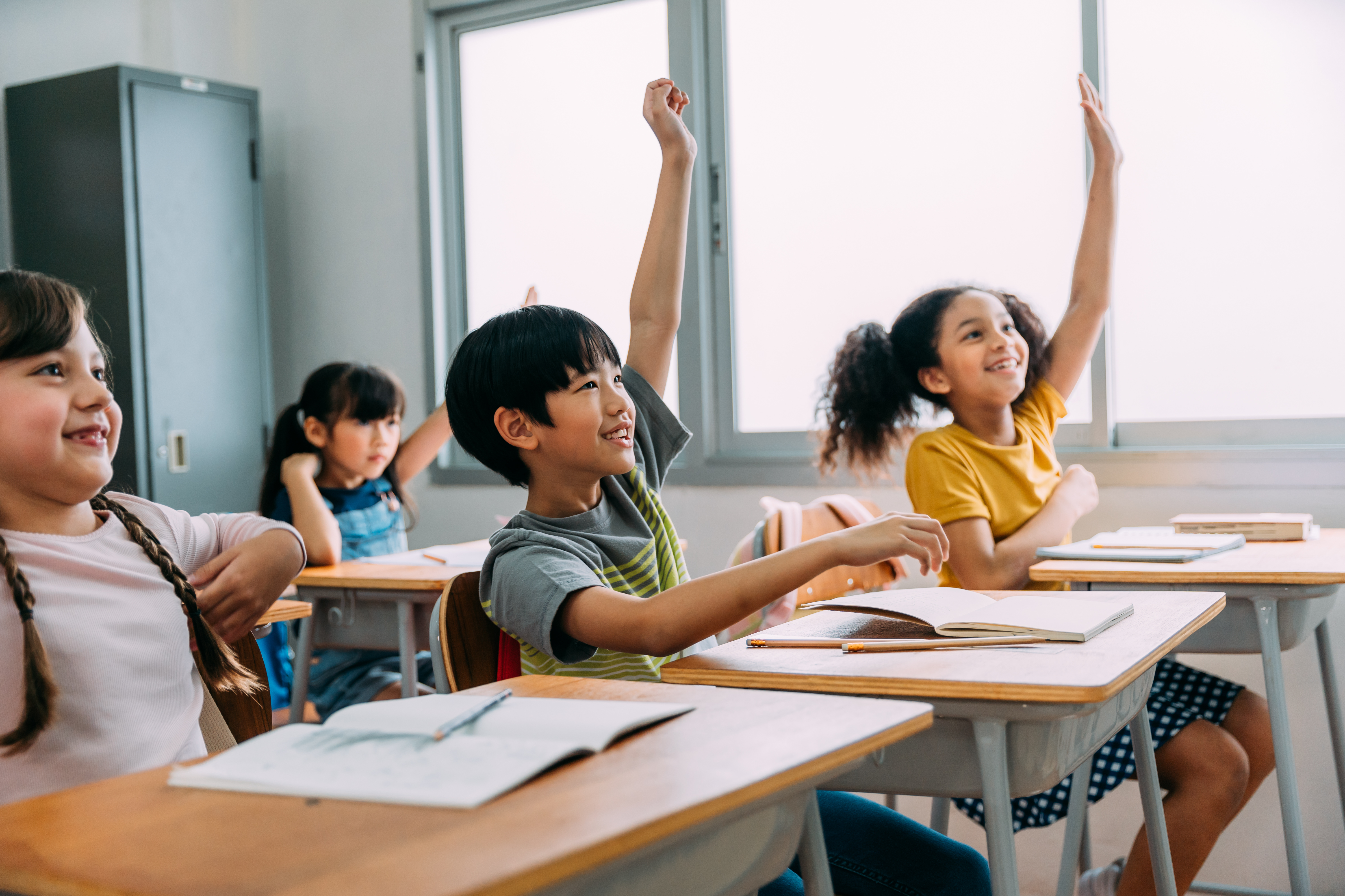 Several middle school students eagerly raise their hands to answer questions