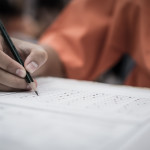 A hand holding a pencil filling out answers on a stardardized test