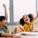 Two students raising their hands and laughing as they look at each other