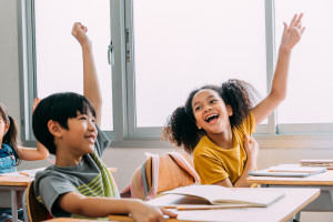 Two students raising their hands and laughing as they look at each other