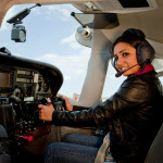 A woman seated in a small airplane cockpit with her hands on the yoke