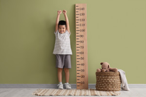 Little Asian boy with stadiometer near green wall