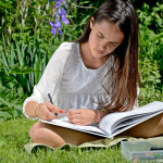 A young girl reads and draws in a garden