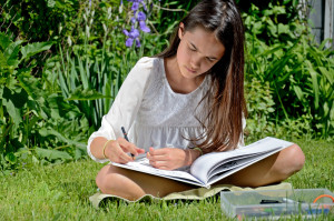 A young girl reads and draws in a garden