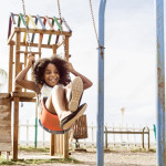 Young girl swinging on a playground swing; a wooden structure behind her