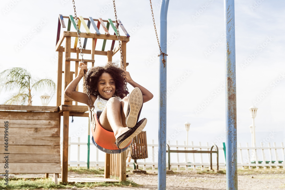 Young girl swinging on a playground swing; a wooden structure behind her